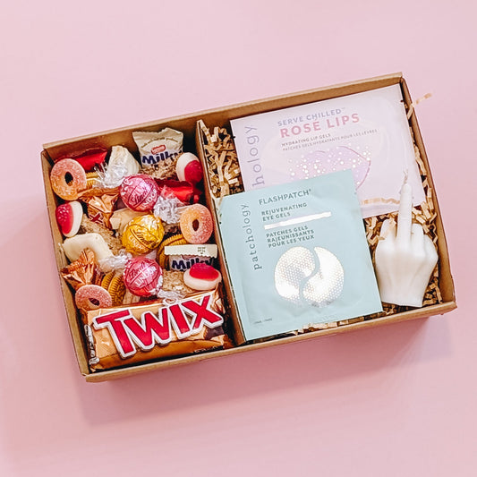Photograph of the better off without him gift pamper hamper from above. The gift box is filled with a patchology eye and lip mask, a rude finger candle and an assortment of pink and gold chocolate, lollies, and cookies. 