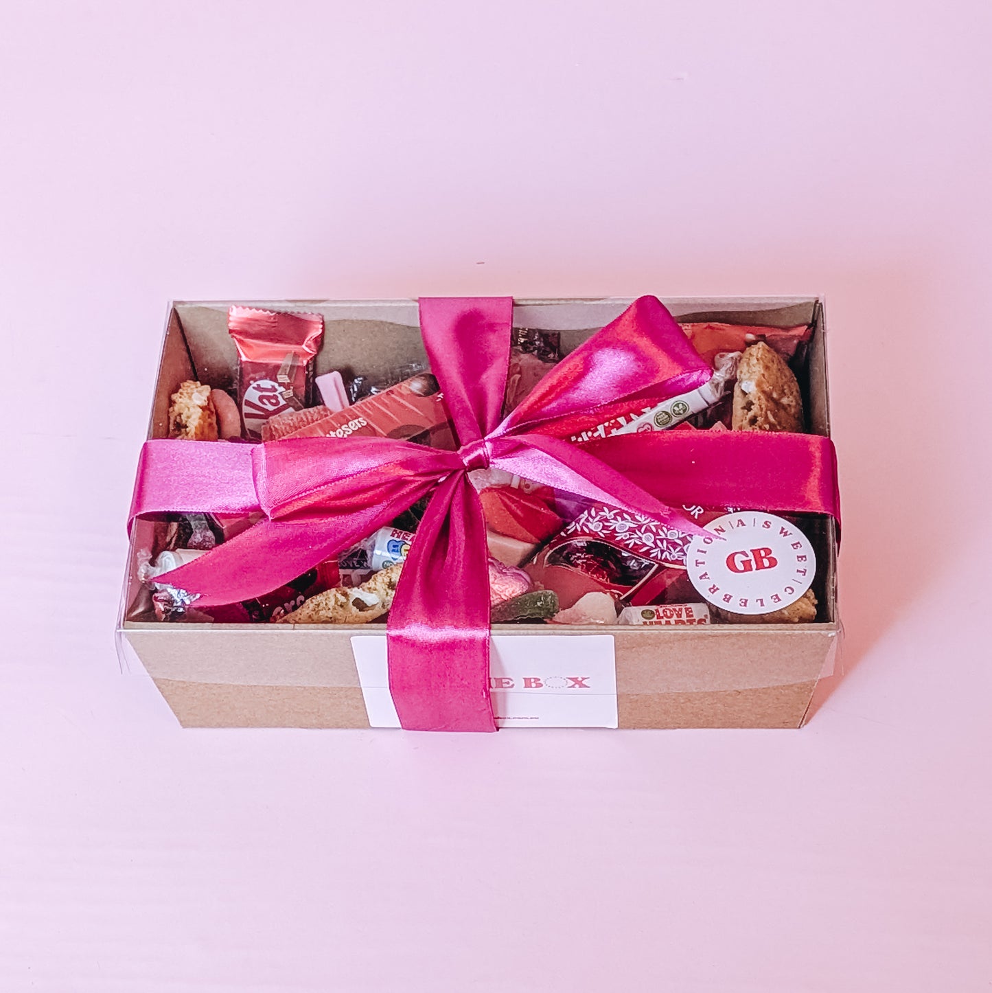 Photograph of Galentines gift hamper. The dessert box is filled with and assortment of valentines themed chocolates, cookies and lollies. Wrapped in a bright pink silk ribbon bow.