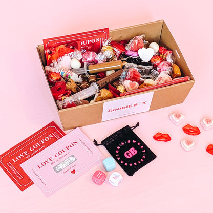 Photograph of valentines gift hamper featuring an assortment of treats including two donuts, lindt chocolates, cookies, nutella and biscoff syringes, love coupons and a black velvet pouch containing dirty dice.