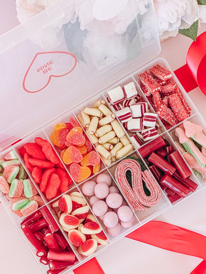 Assorted gummy candies in a box with decorative elements on a light pink background