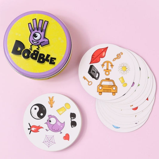 Stack of 'Dobble' game cards with a container on a pink background