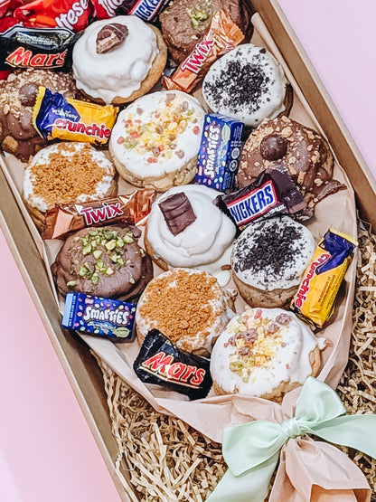 Box of assorted cookies with candy bars on a pink background