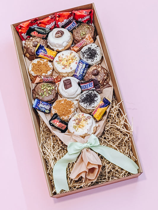 Box of assorted cookies with visible brands on a pink background