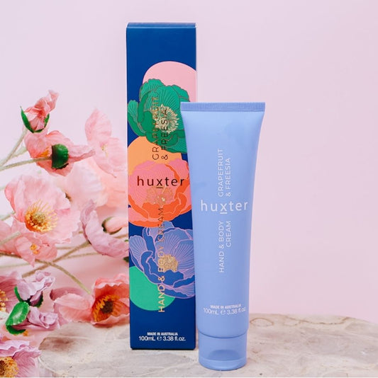 Huxter grapefruit and freesia hand and body cream with floral packaging and flowers in the background