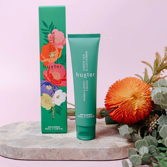 Huxter hand and body cream and packaging with flowers on a pink background