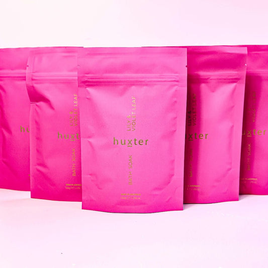 Pink lily and violet leaf bath soak with 'huxter' branding on a pink background