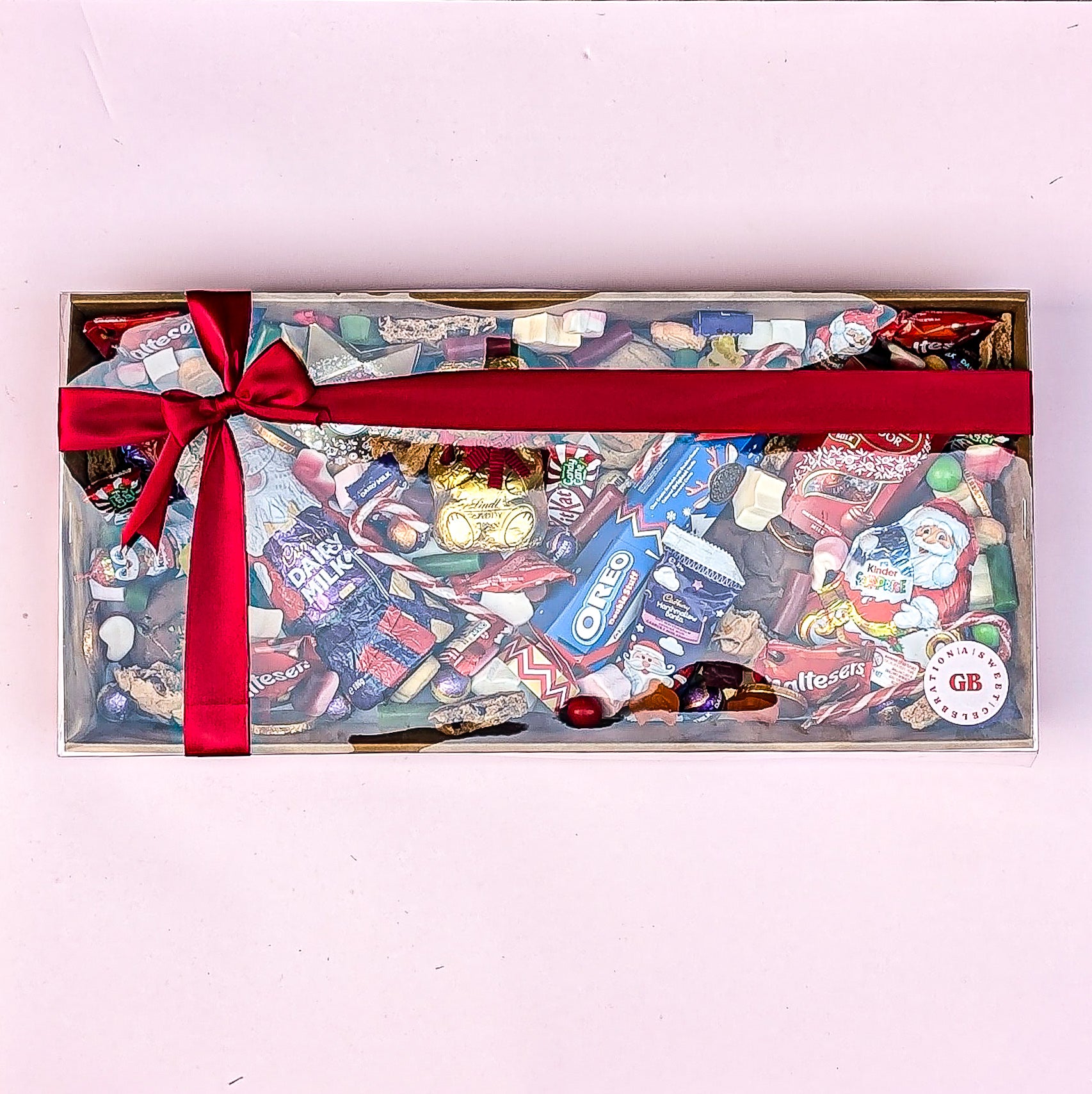 Assorted candy box with a red ribbon on a light pink background