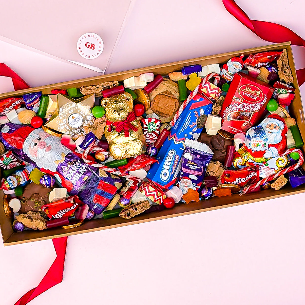 Assorted candy and cookie box with visible brands on a pink background