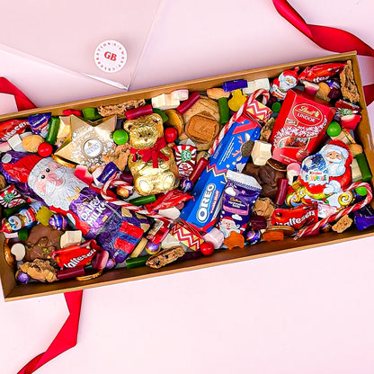 Assorted candy and cookie box with visible brands on a pink background