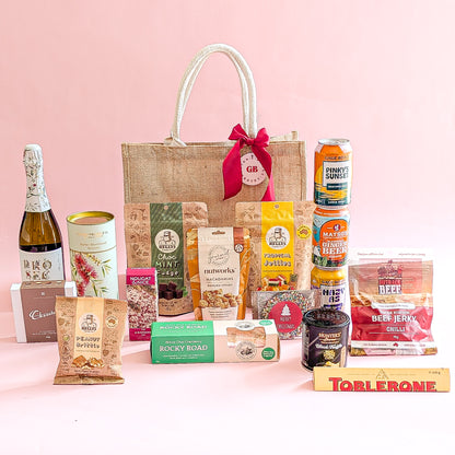 Gift basket with various items including a bottle, snacks, and drinks on a pink background