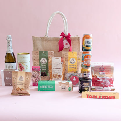 Gift basket with various items including a bottle, snacks, and a can on a pink background