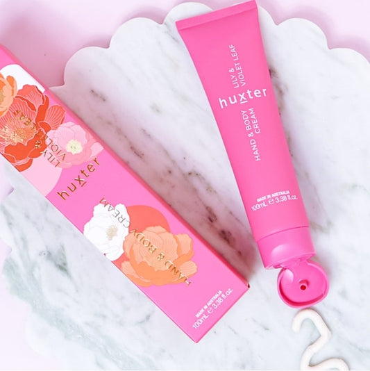 Pink lily and violet lead body and hand cream tube and packaging on a marble surface