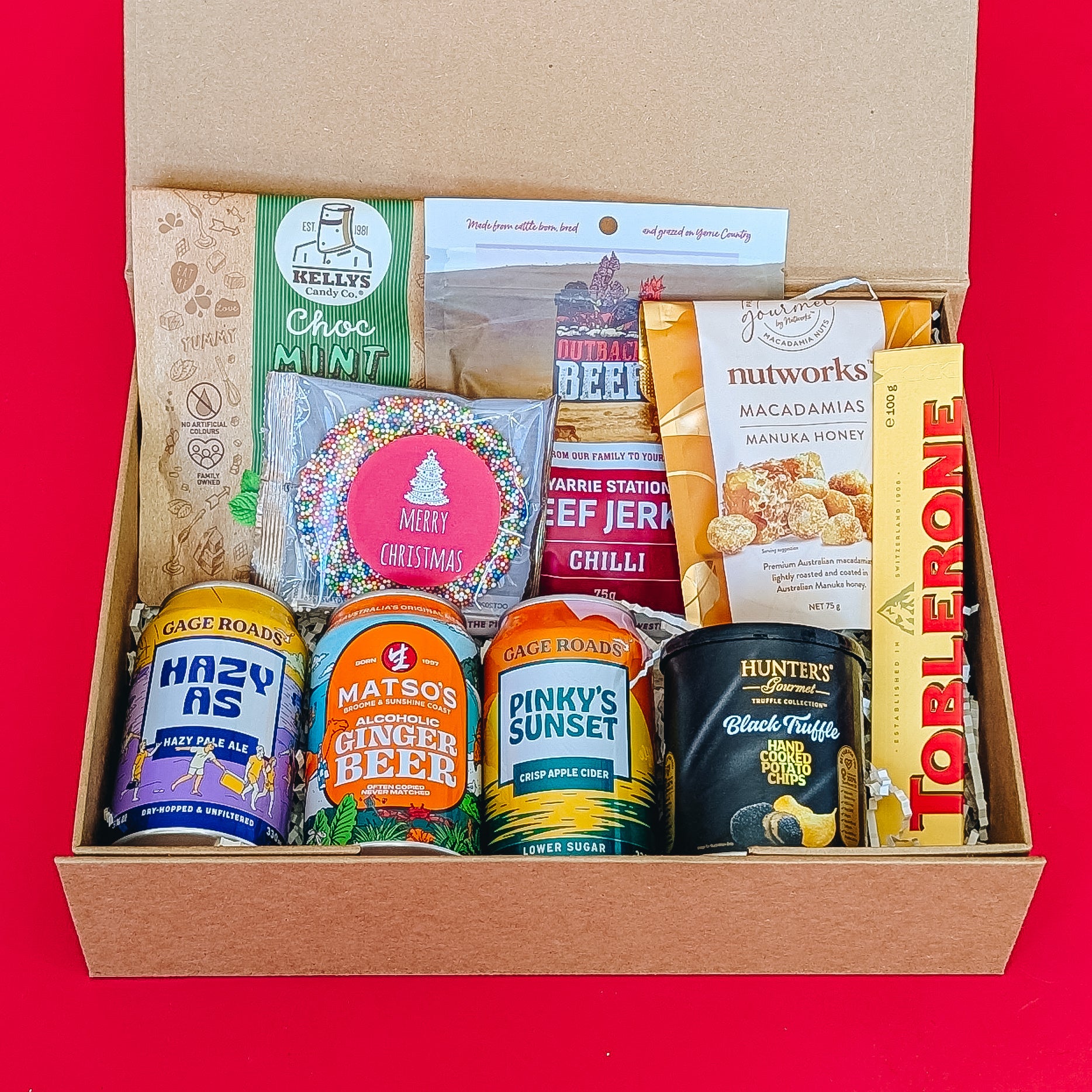 gift hamper with beer, cider and ginger beer with chocolates, beef jerky, crisps and nuts on a red background.