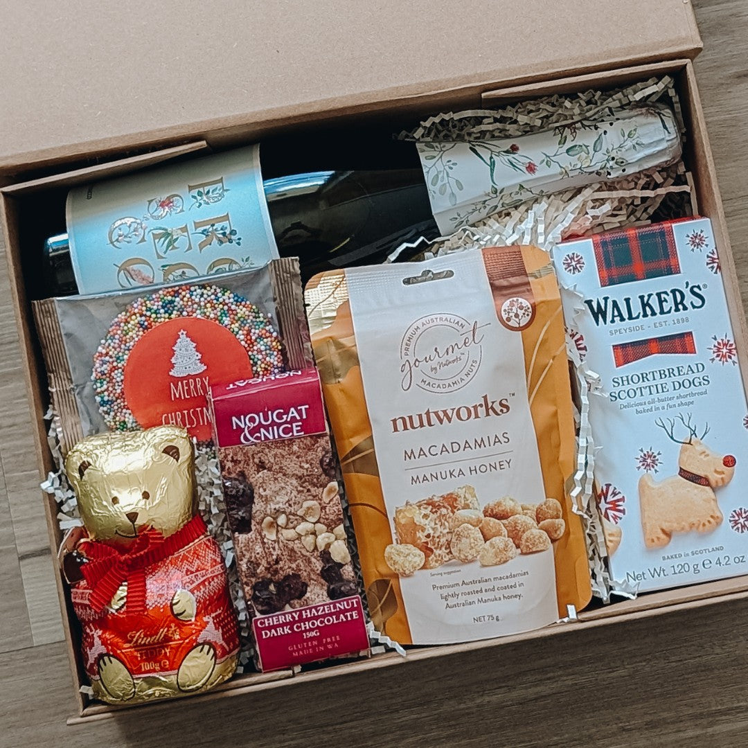 Gift box with bottle of prosecco, buscuits, lindt chocolate and treats on a wooden 
background.