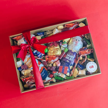 Box of assorted christmas candy with a red ribbon on a red background
