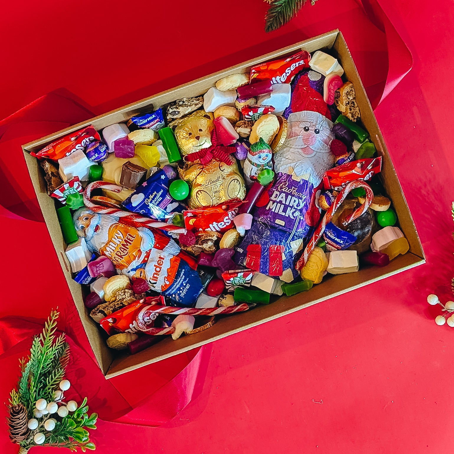 Box of assorted candies including christmas themed chocolate bars and wrapped treats on a red background