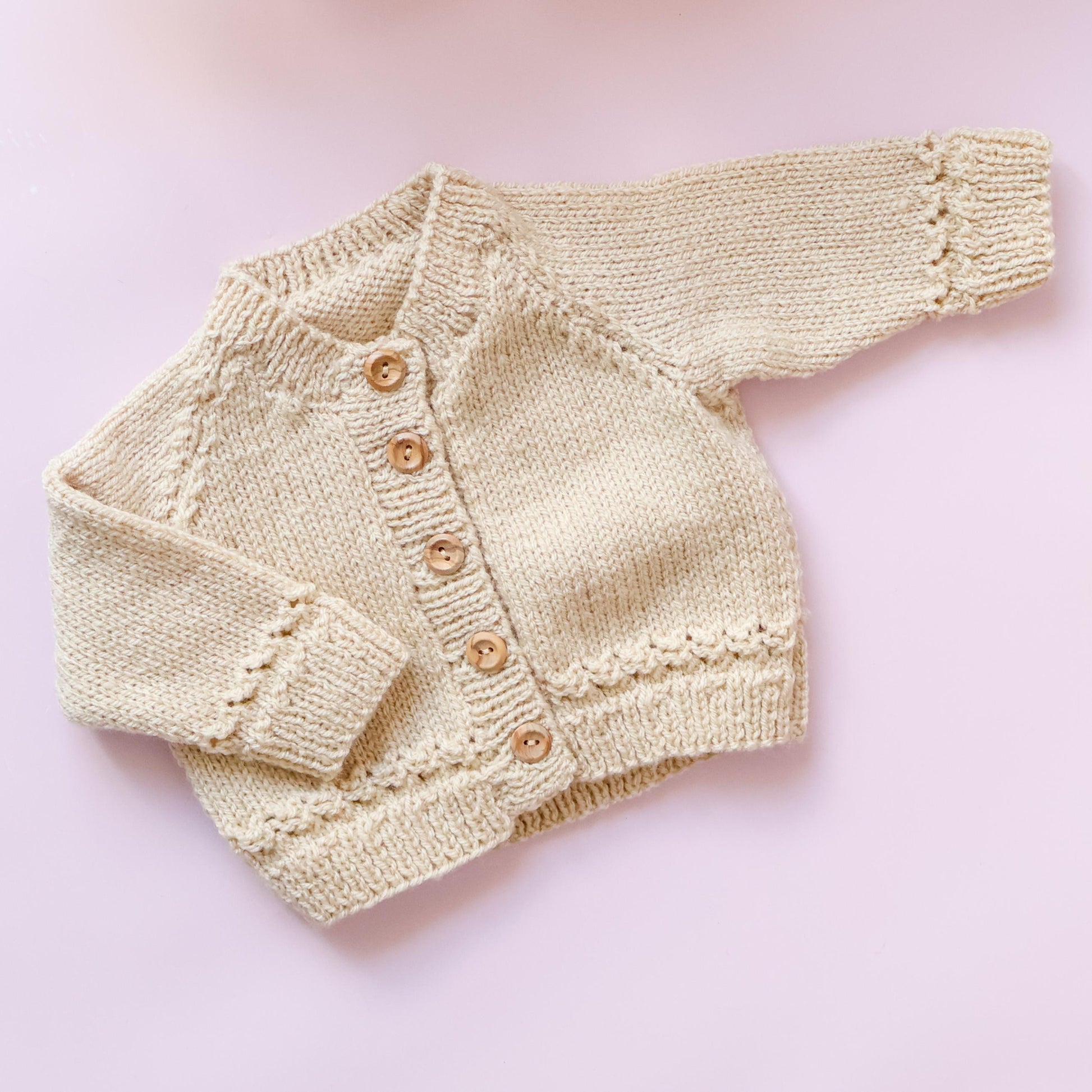 Knitted baby cardigan with buttons on a pink background
