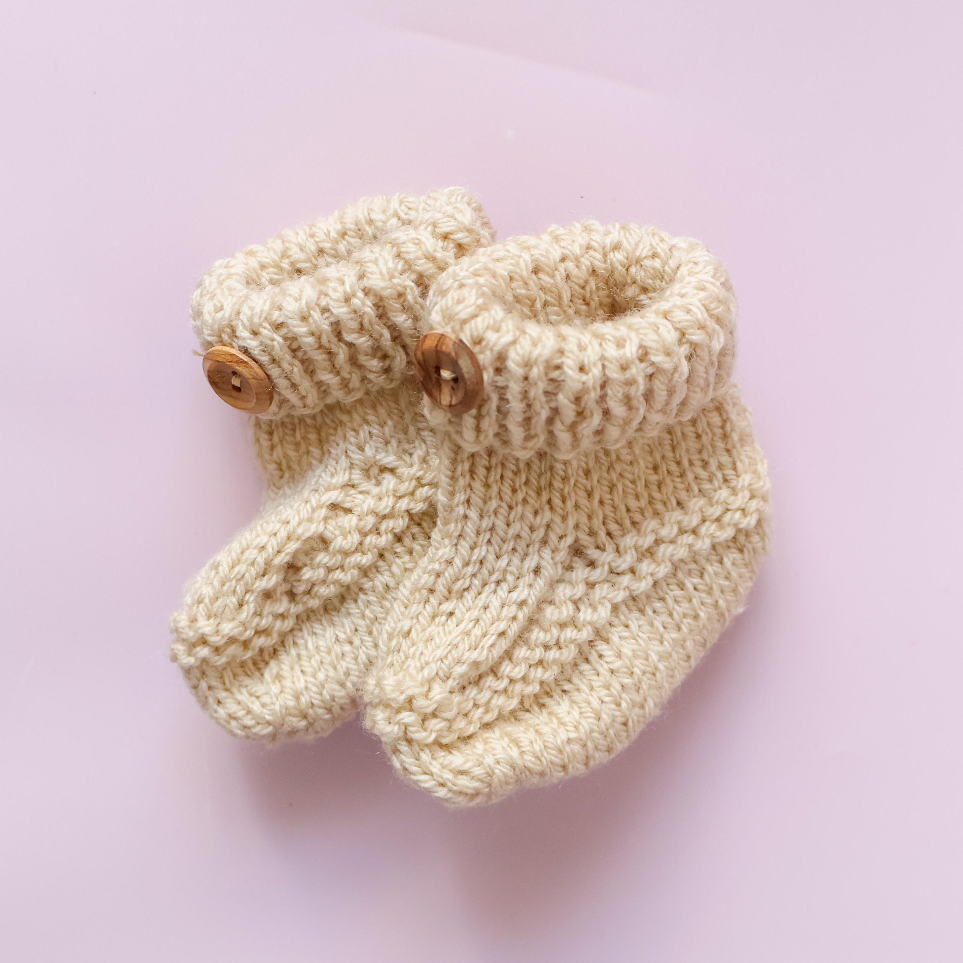 new baby hand knitted booties on a pink backgroun