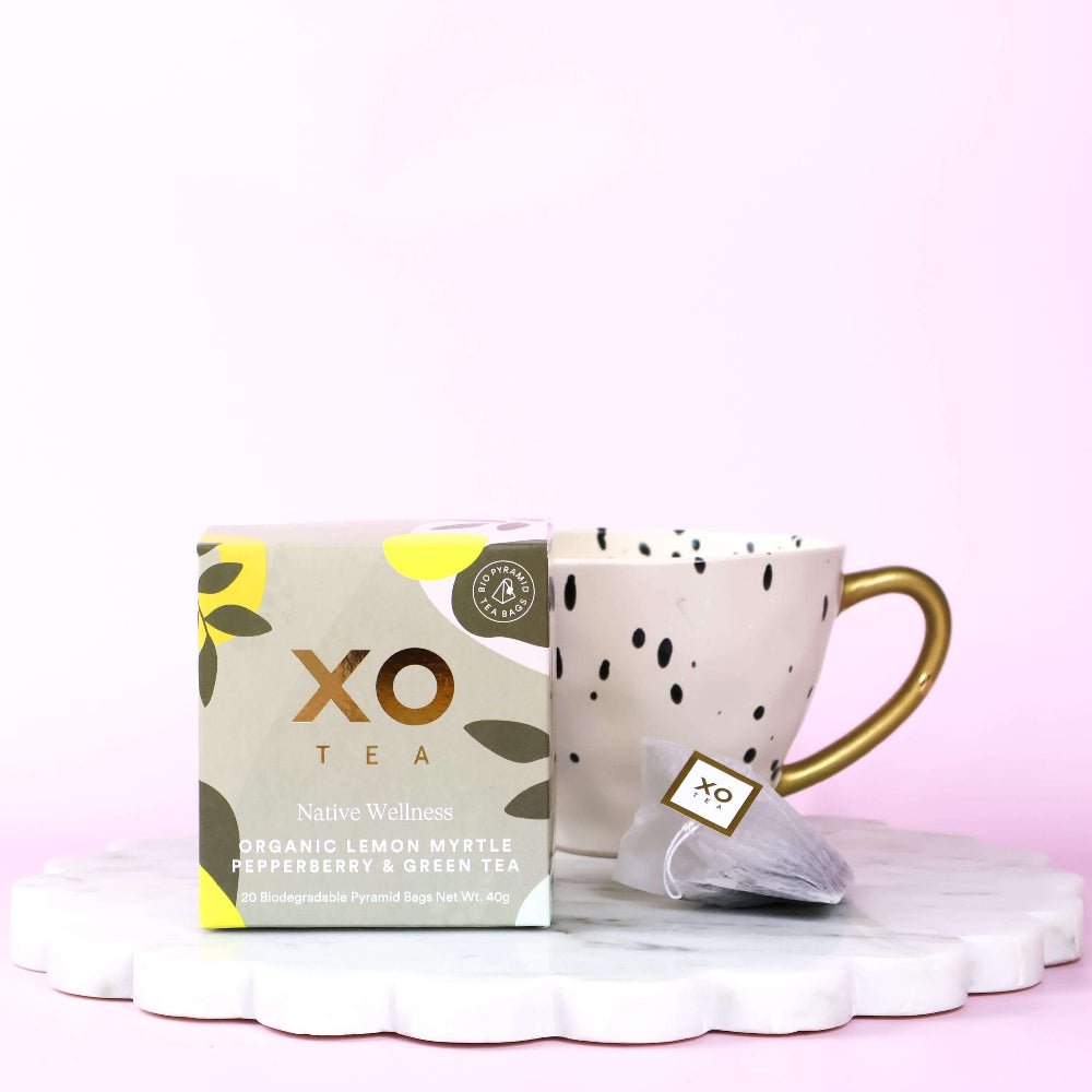 Native Wellness organic lemon myrtle pepperberry and green tea XO Tea box and mug with polka dot design on a white surface with pink background