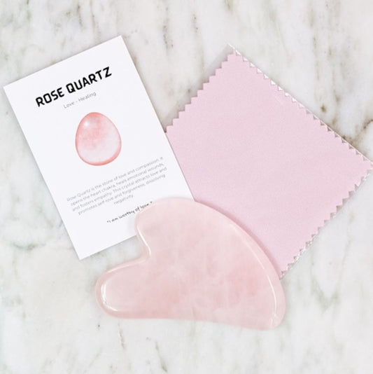 Rose quartz gua sha tool with a pink cloth and information card on a marble surface