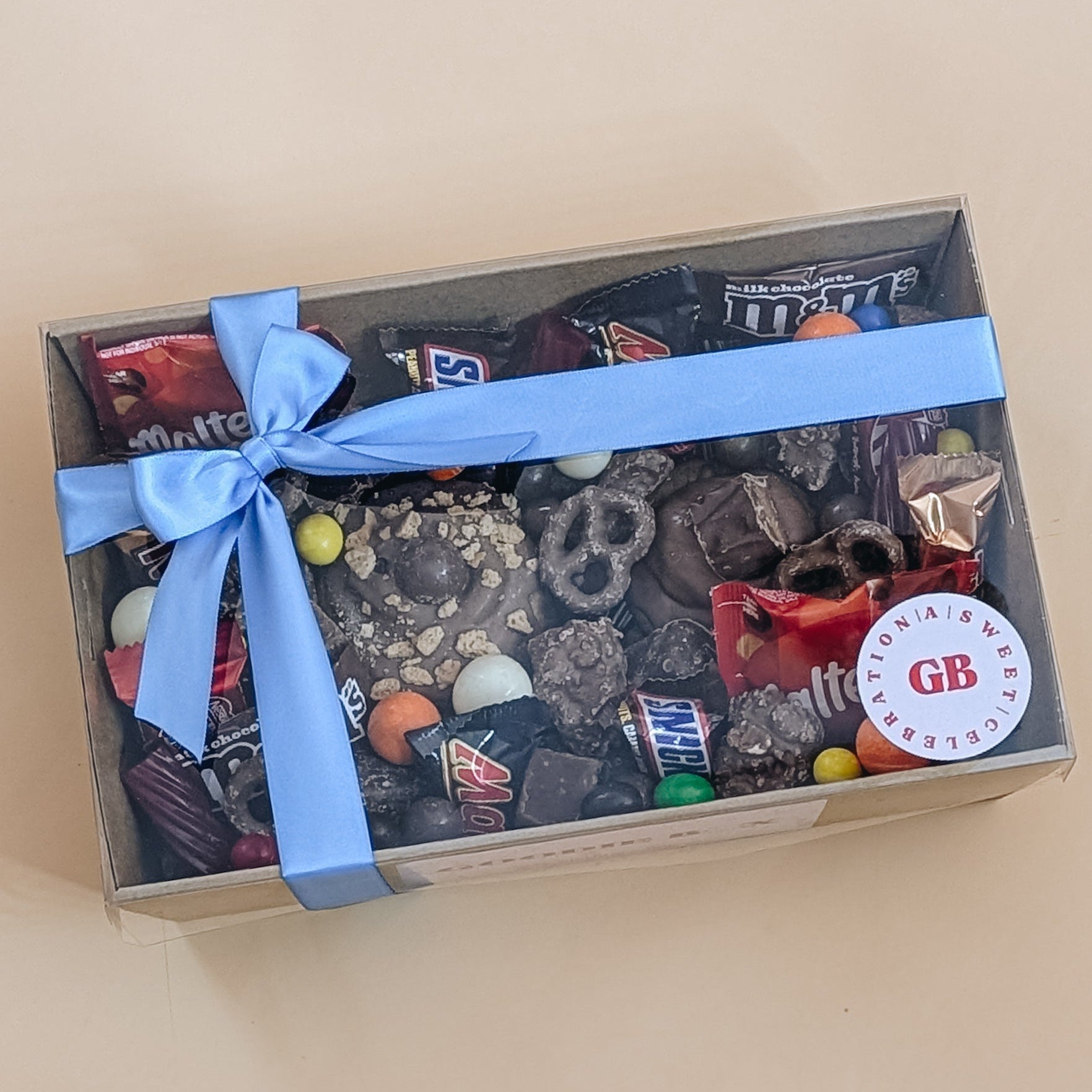 Box of assorted candy with a blue ribbon on a beige background