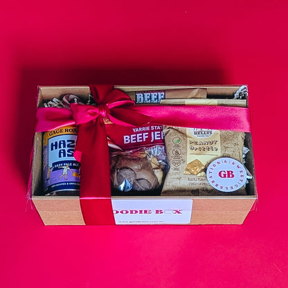corporate gift box with beef jerkie, pale ale peanut brittle and cookie with a red ribbon on a red background.