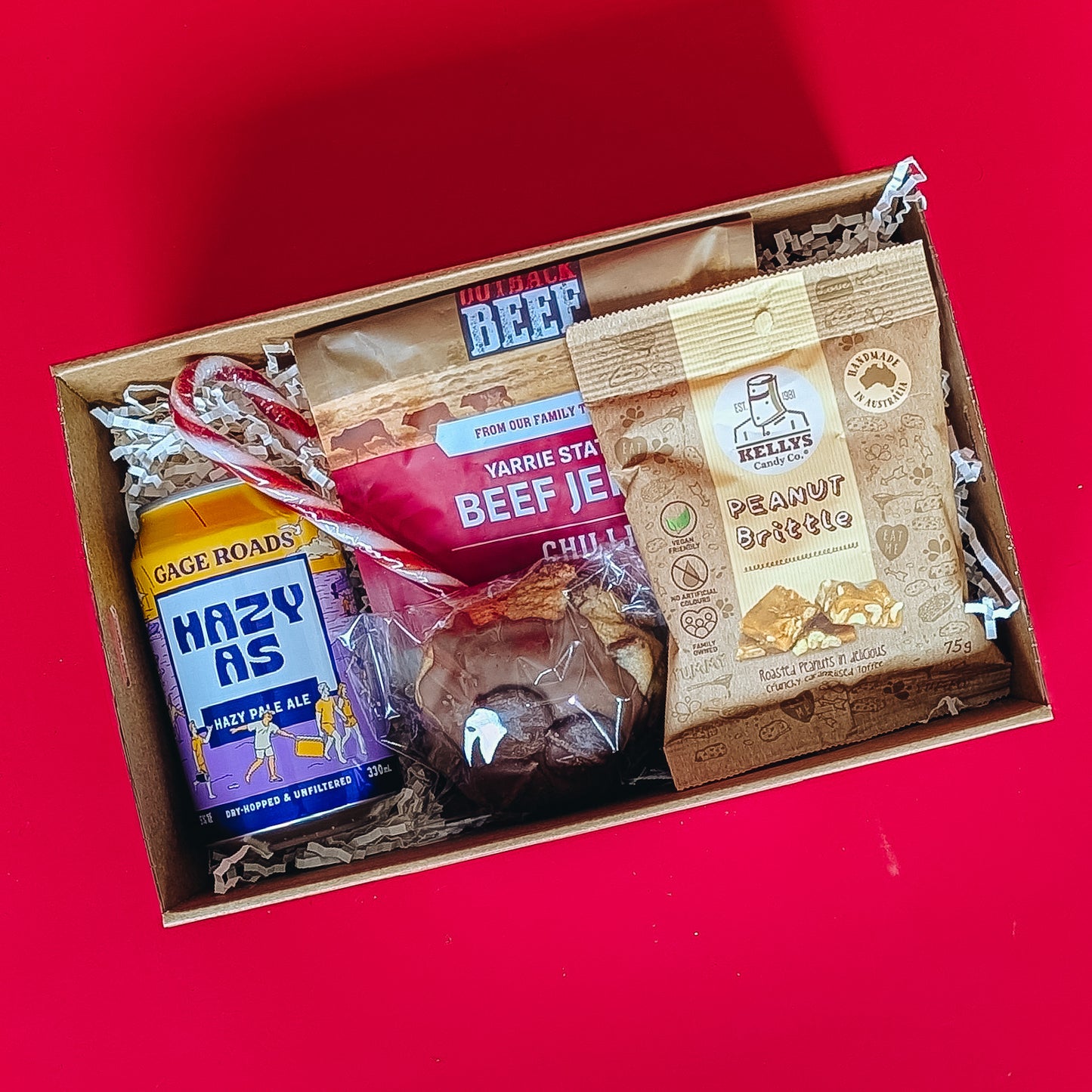 corporate gift box with beef jerkie, pale ale peanut brittle and cookie on a red background.