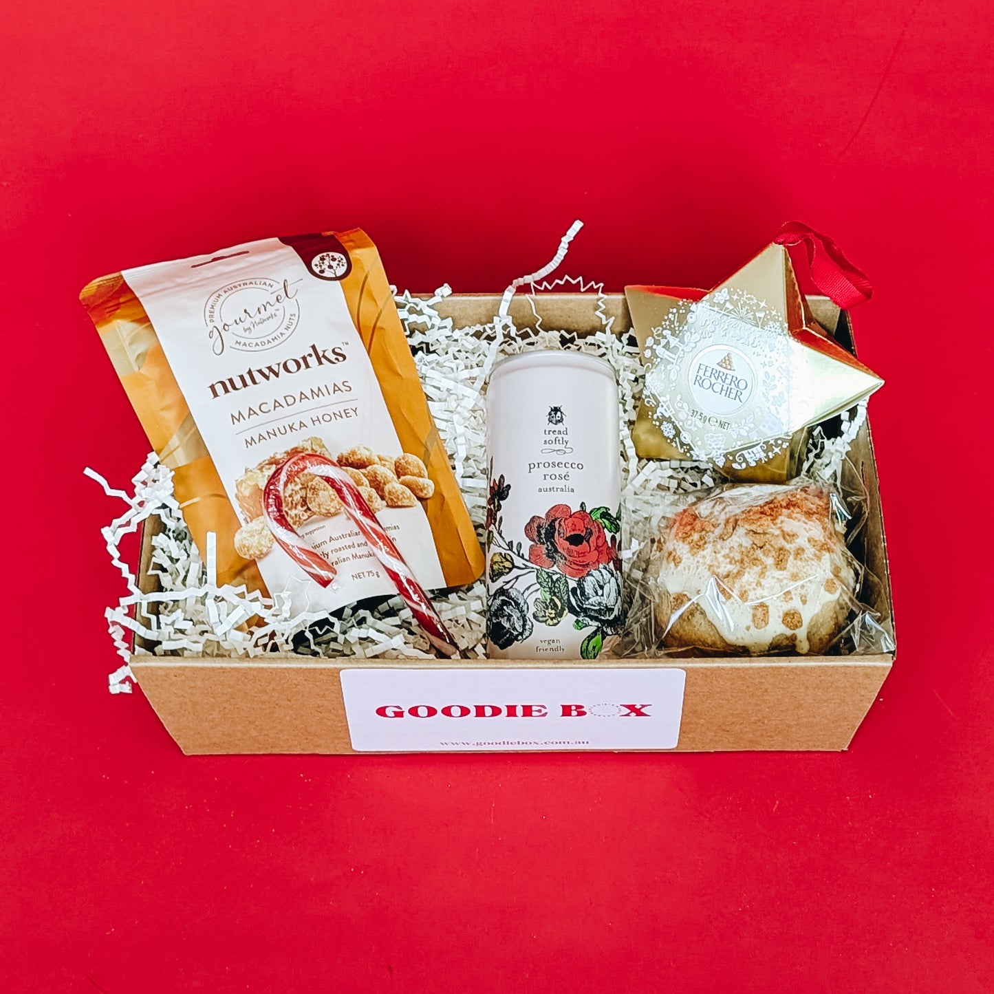 Gift box with assorted items including cookies, ferrero rocher, honey nuts and  sparkling wine on a red background