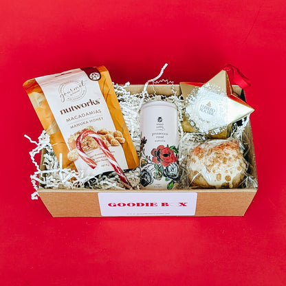 Gift box with assorted items including cookies, ferrero rocher, honey nuts and  sparkling wine on a red background