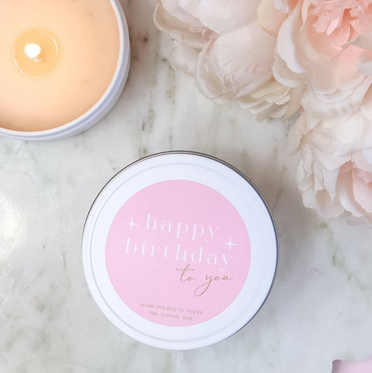 Candle in a tin with 'happy birthday to you' text on a marble surface with flowers.