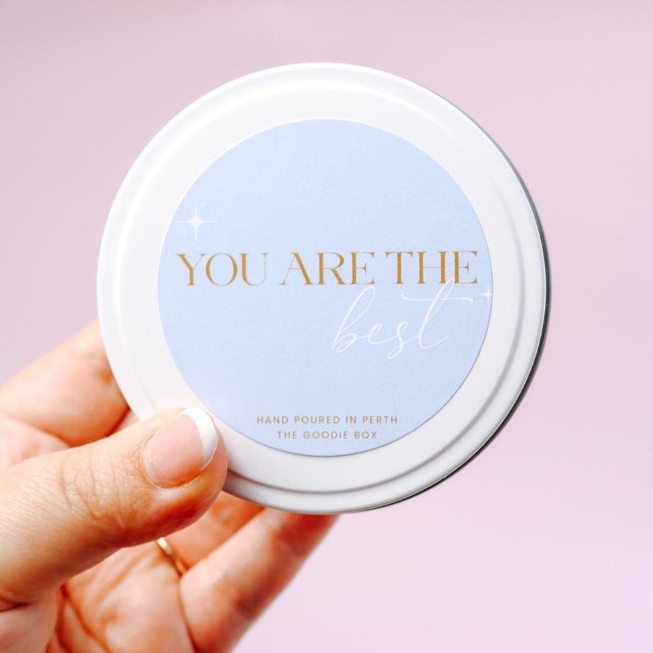 Hand holding a candle tin with 'You are the best' text on a light purple background