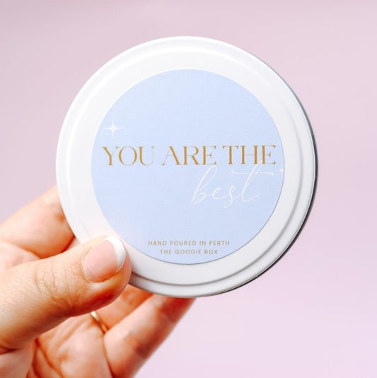 Hand holding a candle tin with 'You are the best' text on a light purple background