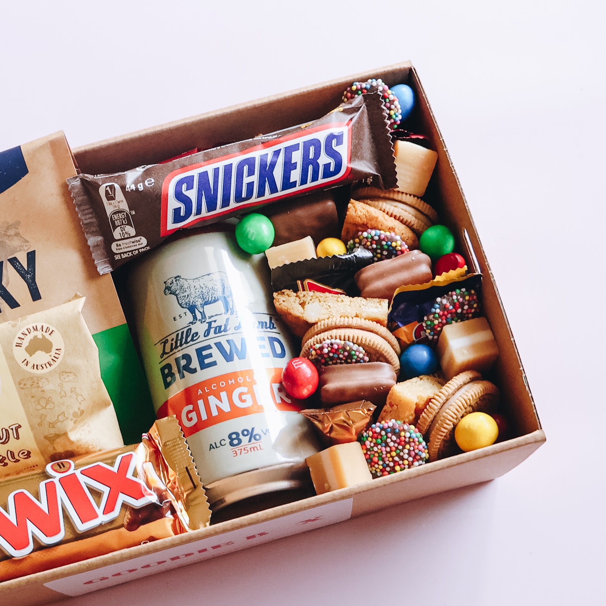 Goodie Box sweet and savoury treat box close up showing Little Fat Lamb ginger beer, Snickers, Twix, Kelly's Peanut Brittle and Beef Jerky on grey background Perth