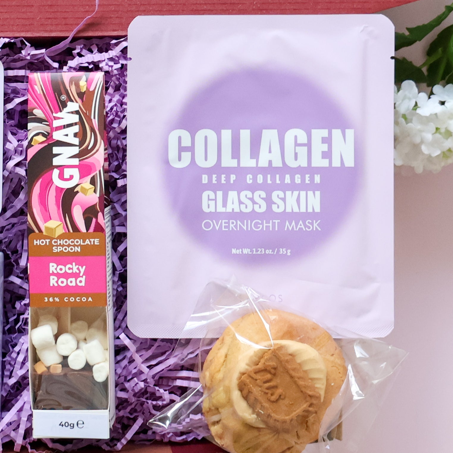 Care Package detail showing Gnaw rocky road hot chocolate spoon Lapcos collagen glass skin overnight mask and loaded filled cookie
