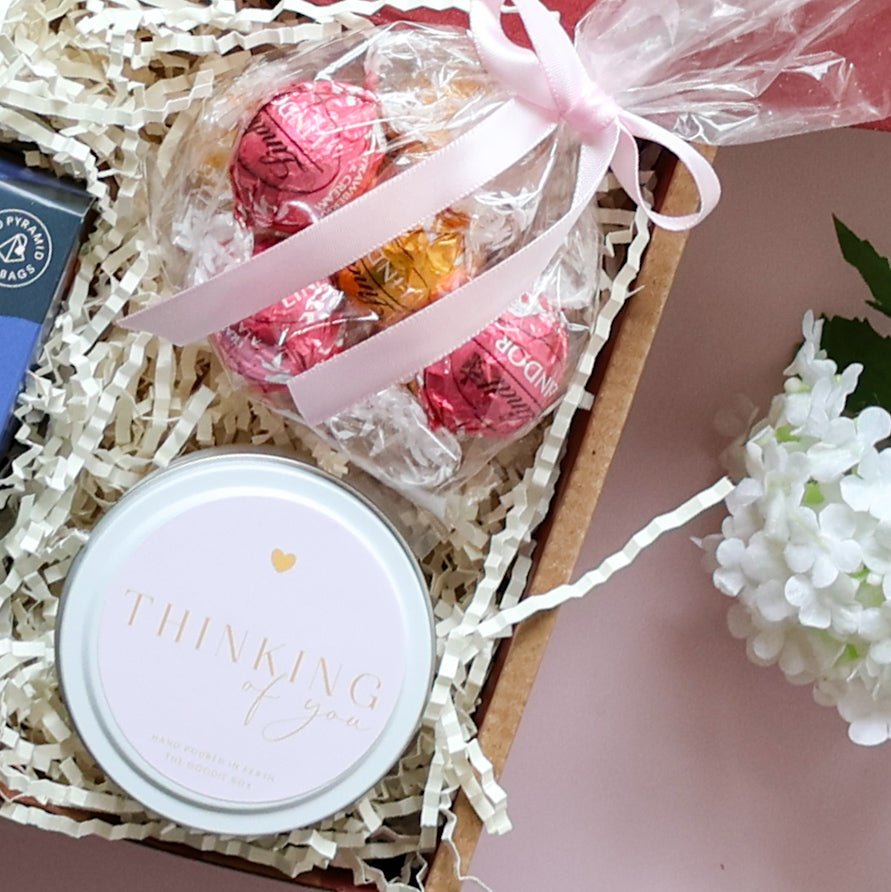 Thinking of you gift box showing Thinking of You soy candle tin Lindt Lindor chocolates and pink ribbon on pink background