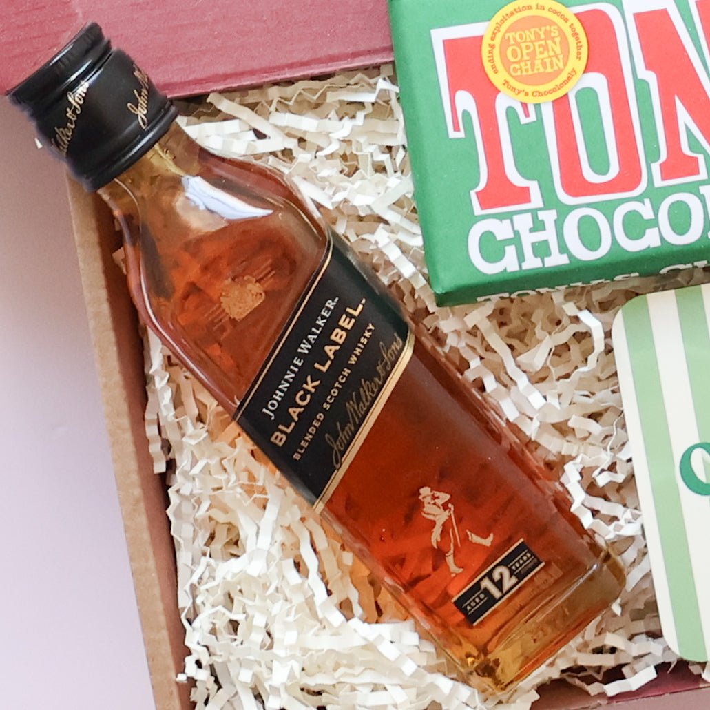 Close up of Johnnie Walker Black Label whisky bottle in thoughtful gift for him with Tony's Chocolonely chocolate hazelnut