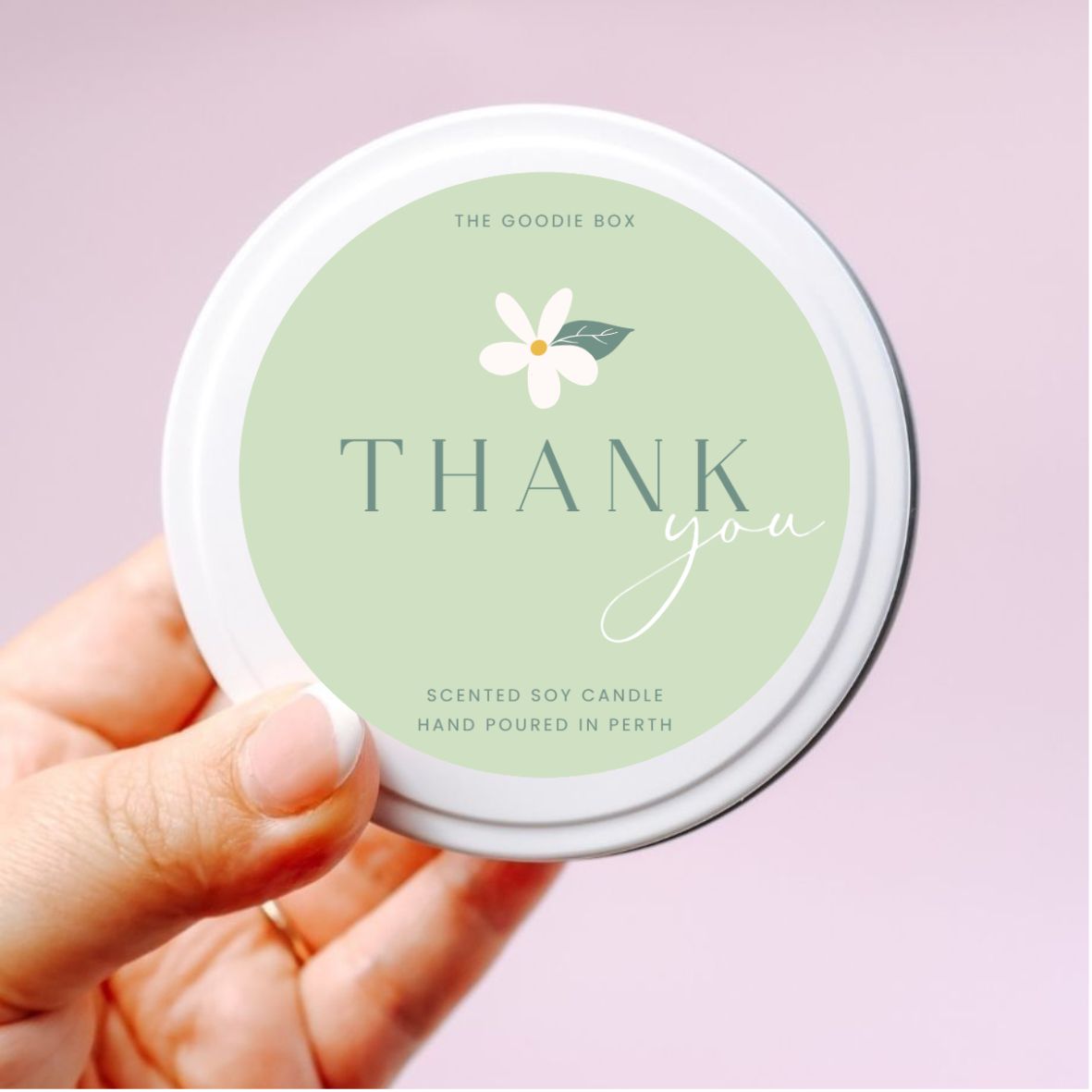 photo of a hand holding a white soy candle tin with green sticker reading "thank you" with white flower